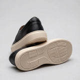 Mocassim Slip On Casual de Couro: par preto com um sapato virado, mostrando a sola bege com sulcos.