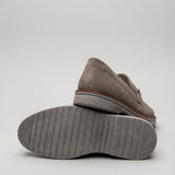 Par do modelo Mocassim Suede Tratorado de Camurça, na cor cinza, com um dos solados voltado para a câmera.