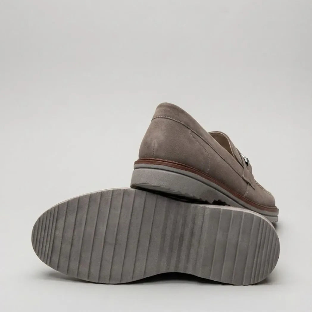 Par do modelo Mocassim Suede Tratorado de Camurça, na cor cinza, com um dos solados voltado para a câmera.