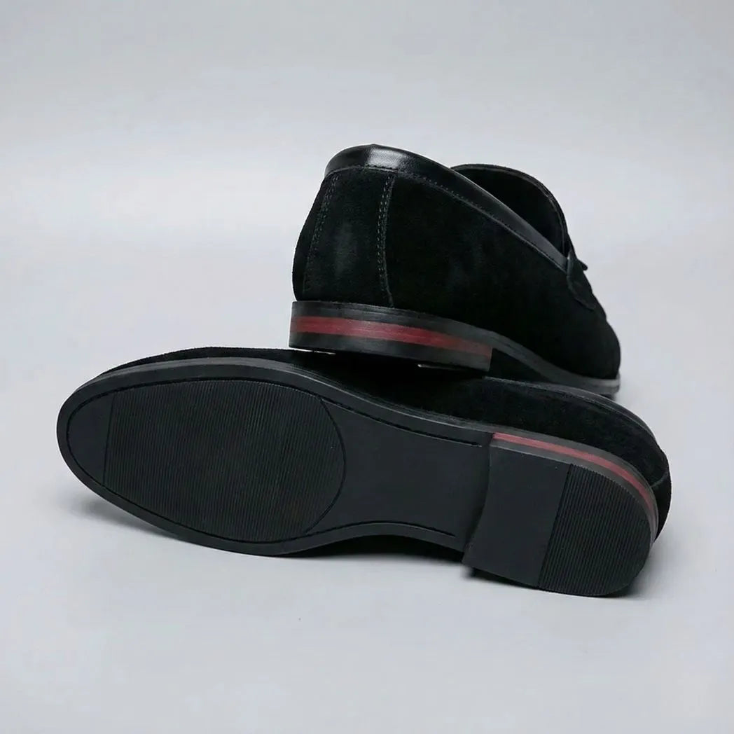 Mocassim Tassel de Camurça Premium: par preto com um sapato virado, mostrando a sola escura e o detalhe vermelho no salto.