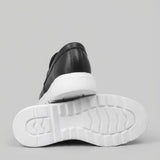 Par do modelo Mocassim Torino Ripple Tratorado de Couro, na cor preto, com um dos solados voltado para a câmera.