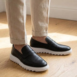 Mocassim Torino Ripple Tratorado de Couro na cor preto, usado com calça clara de barra dobrada.