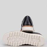Par do modelo Mocassim Tratorado Milano de Couro, na cor preto, com um dos solados voltado para a câmera.