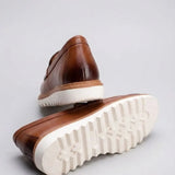 Par do modelo Mocassim Tratorado Milano de Couro, na cor marrom, com um dos solados voltado para a câmera.