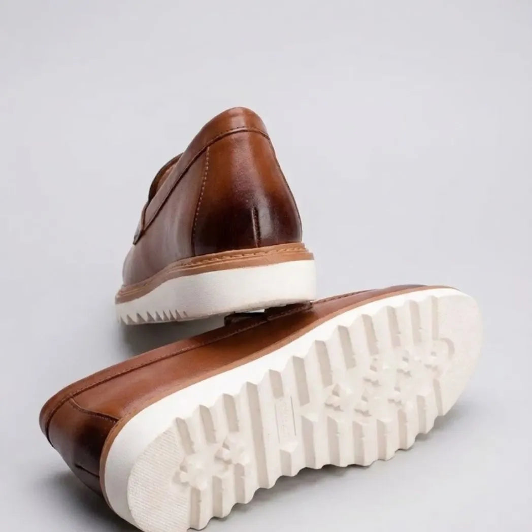 Par do modelo Mocassim Tratorado Milano de Couro, na cor marrom, com um dos solados voltado para a câmera.