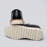 Par do modelo Mocassim Tratorado Siena Ripple, na cor preto, com um dos solados voltado para a câmera.