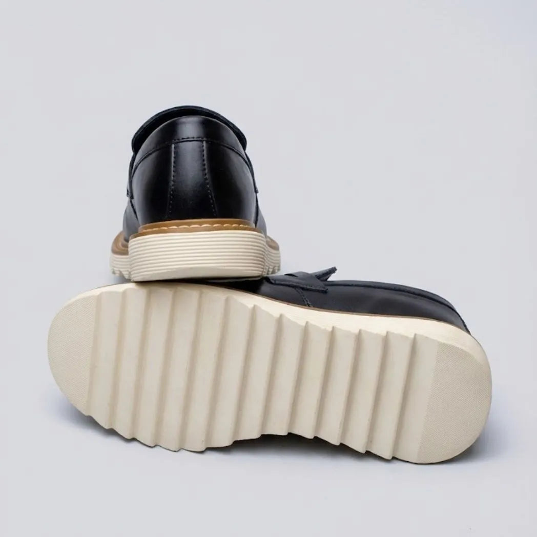 Par do modelo Mocassim Tratorado Siena Ripple, na cor preto, com um dos solados voltado para a câmera.