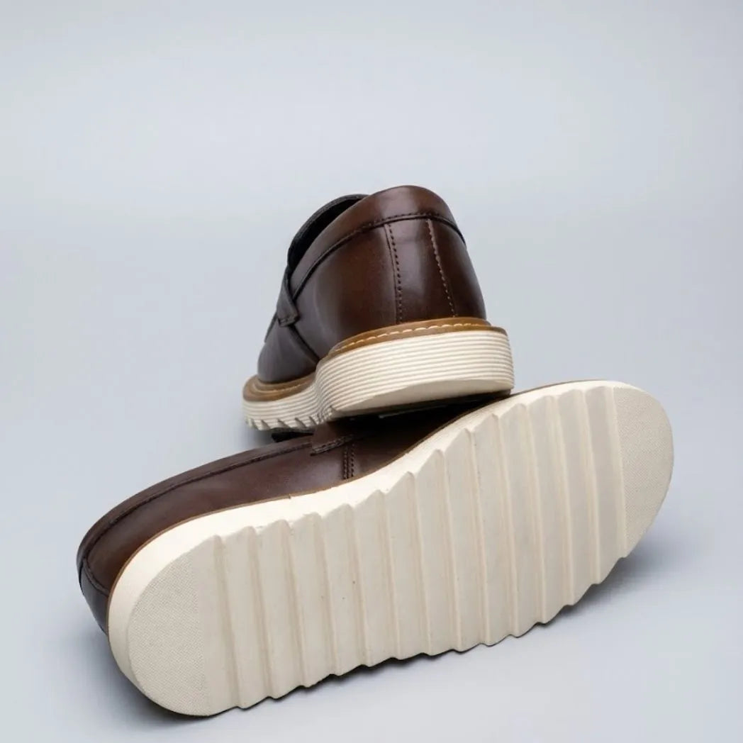 Par do modelo Mocassim Tratorado Siena Ripple, na cor marrom, com um dos solados voltado para a câmera.