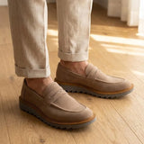 Mocassim Tratorado Taupe de Camurça na cor bege, usado com calça clara de barra dobrada.