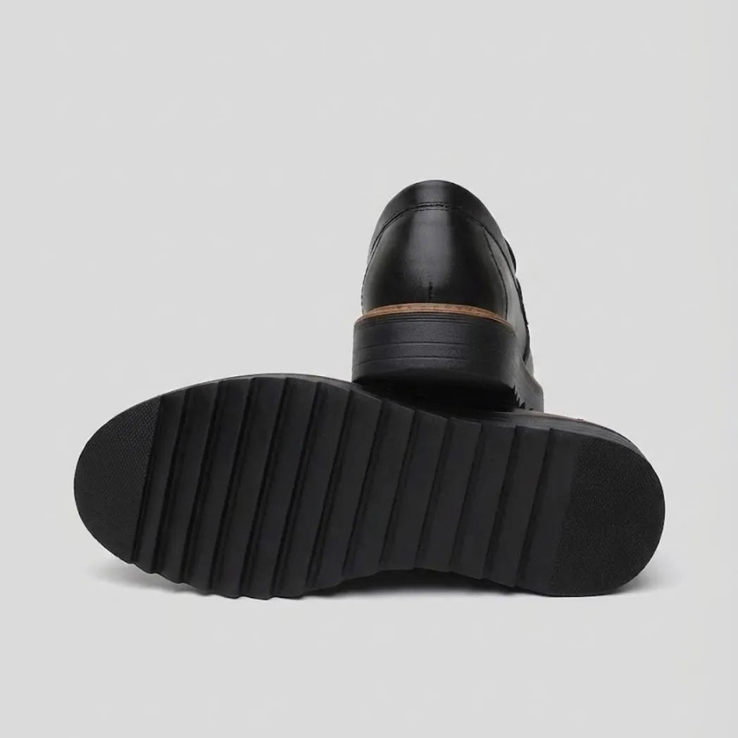 Par do modelo Mocassim Tratorado Torino Ripple, na cor preto, com um dos solados voltado para a câmera.