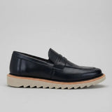 Mocassim Tratorado de Couro Verona: modelo preto de perfil, com faixa frontal, borda marrom e sola bege com sulcos profundos.