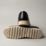 Par do modelo Mocassim Tratorado de Couro Verona, na cor preto, com um dos solados voltado para a câmera.