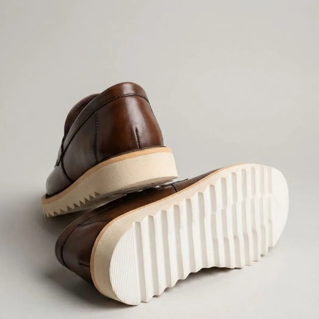 Par do modelo Mocassim Tratorado de Couro Verona, na cor marrom, com um dos solados voltado para a câmera.
