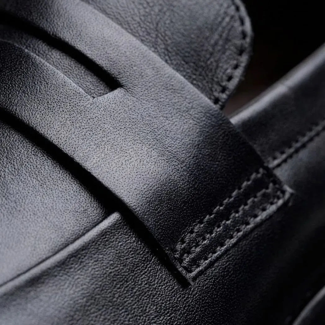 Mocassim Turim Loafer Couro: detalhe da superfície preta, da faixa frontal e da costura lateral.