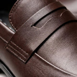 Mocassim Turim Loafer Couro: detalhe da superfície marrom-escura, da faixa frontal e da costura.