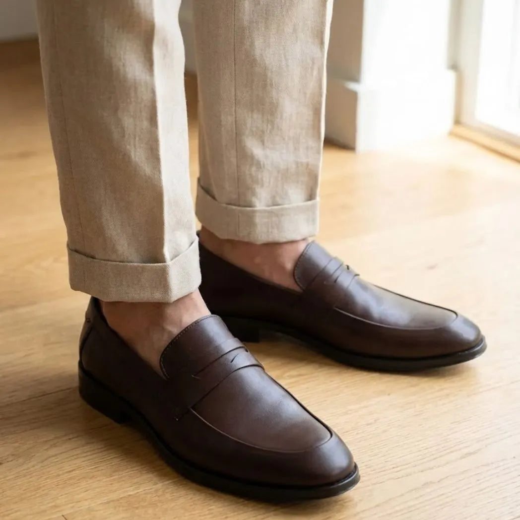 Mocassim Turim Loafer Couro: par marrom-escuro usado com calça clara dobrada na barra.