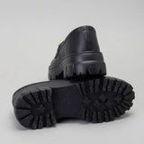 Par do modelo Mocassim Vanguard Tratorado, na cor preto, com um dos solados voltado para a câmera.