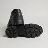 Par do modelo Mocassim Vanguard Tratorado, na cor preto, com um dos solados voltado para a câmera.