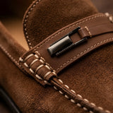 Detalhe da ferragem retangular escura, da faixa de couro marrom e das costuras do Mocassim de Camurça Titan Coffee Marrom.