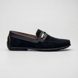 Mocassim de Camurça Titan Coffee: modelo preto de perfil, com ferragem retangular na faixa frontal e sola preta.