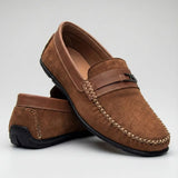 Mocassim de Camurça Titan Coffee: par marrom em posição cruzada, com ferragem na faixa frontal e costura clara.
