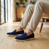 Mocassim de Camurça de Lebre: par azul-escuro com sola clara usado com calça bege, com a pessoa sentada em cadeira.