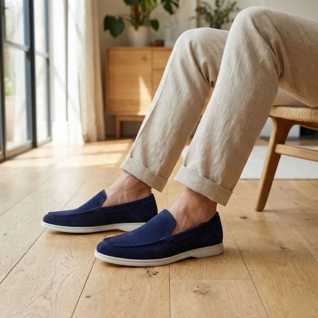 Mocassim de Camurça de Lebre: par azul-escuro com sola clara usado com calça bege, com a pessoa sentada em cadeira.