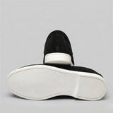 Mocassim de Camurça: par preto com um sapato virado, mostrando a sola branca.