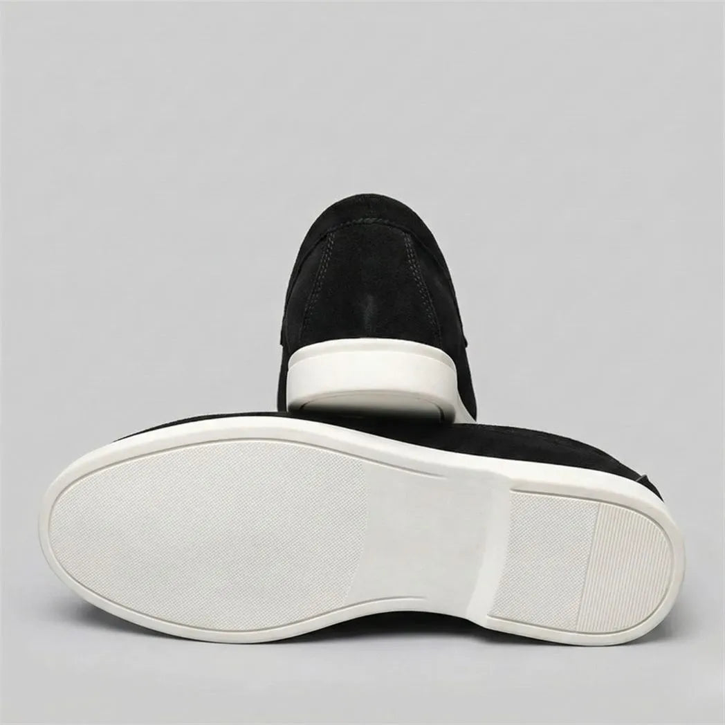 Mocassim de Camurça: par preto com um sapato virado, mostrando a sola branca.