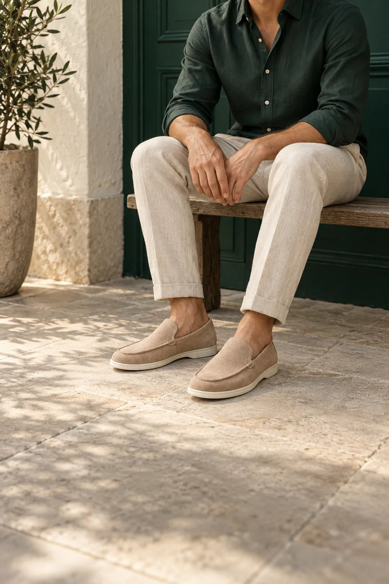 Campanha Louford: homem sentado em banco de madeira, com camisa verde, calça clara e mocassins de camurça bege, em fotografia vertical.